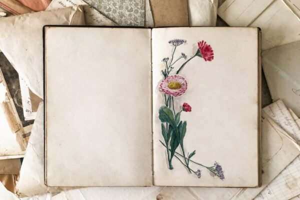 blank journal with flowers on page lying on old photos and papers