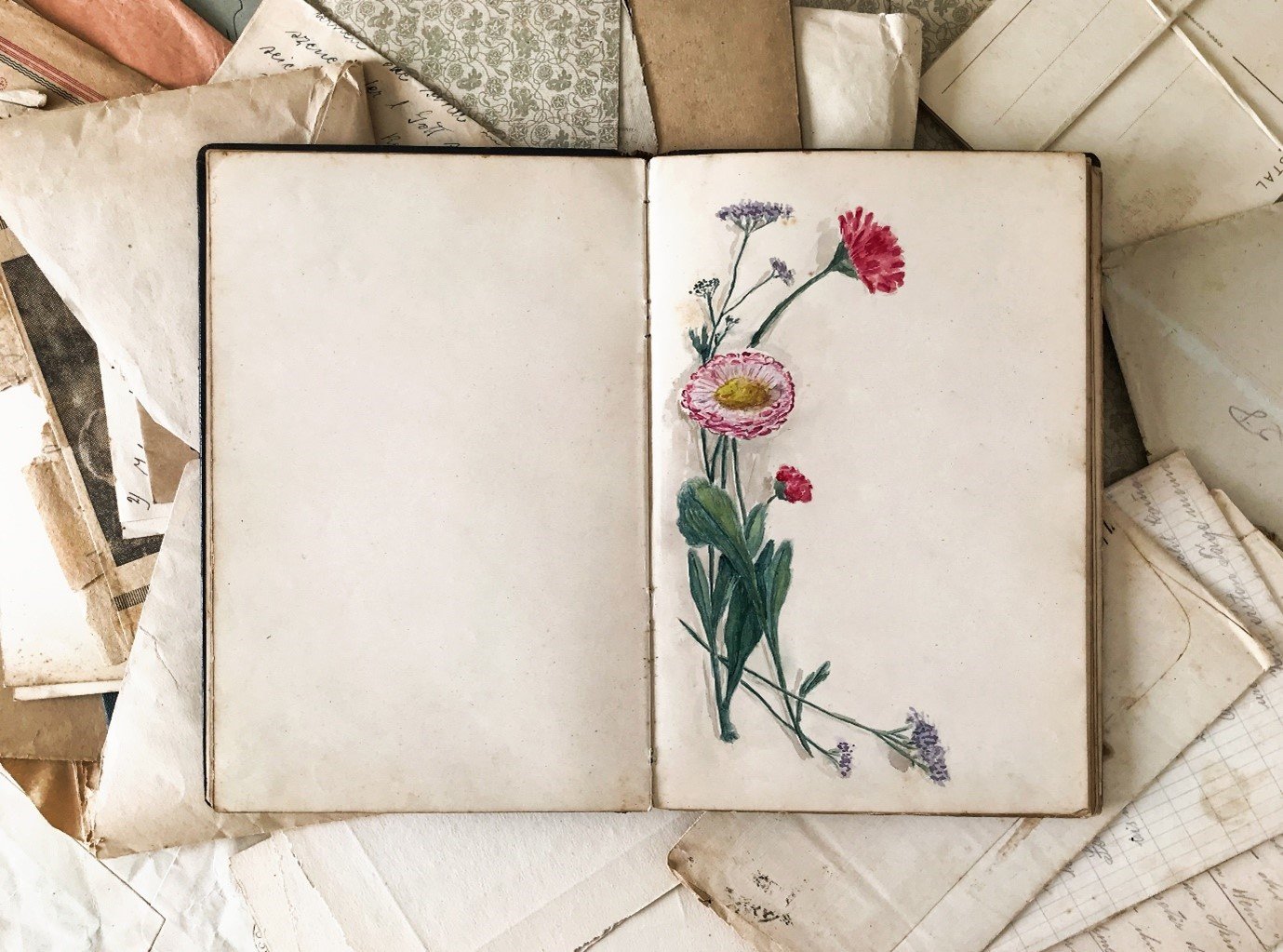 blank journal with flowers on page lying on old photos and papers