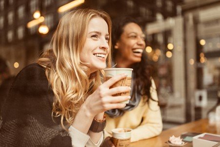 two women laughing while drinking coffee